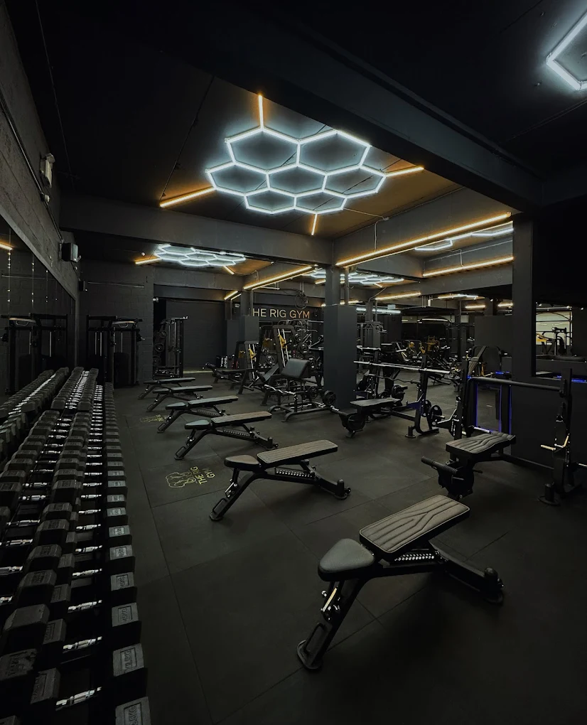The Rig Gym, Epsom — training floor at night with hexagonal LED lighting and dumbbell racks